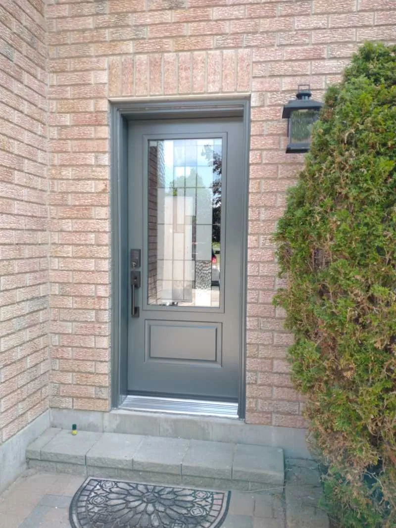 Grey steel front door with a decorative glass insert on a brick home, installed by Panorama Windows & Doors Grey steel front door with a decorative glass insert on a brick home