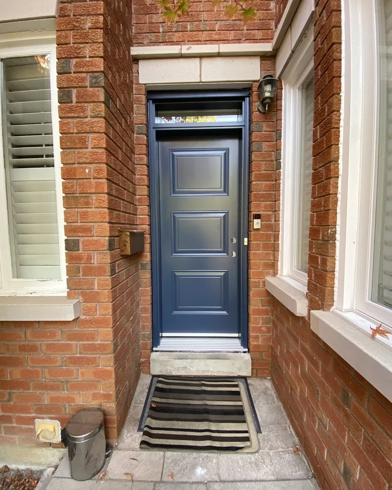 White Six-Panel Door to Navy Steel Door: after Front door with a transom on a brick wall after replacement