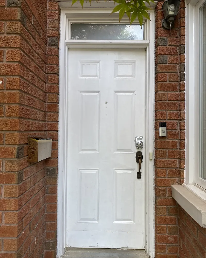 White Six-Panel Door to Navy Steel Door: before Front door with a transom on a brick wall before replacement